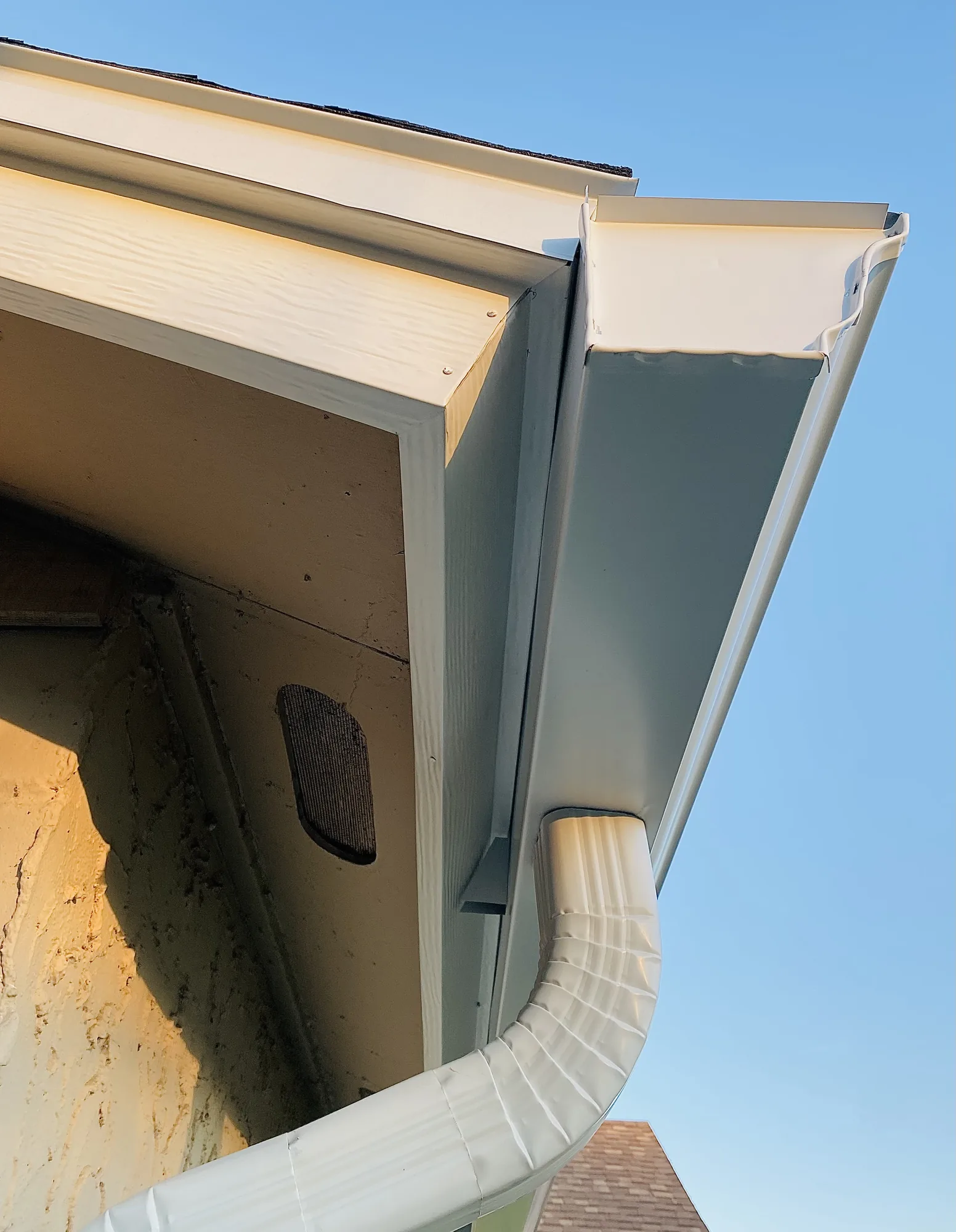 Close view of a white gutter, fascia and downspout connection